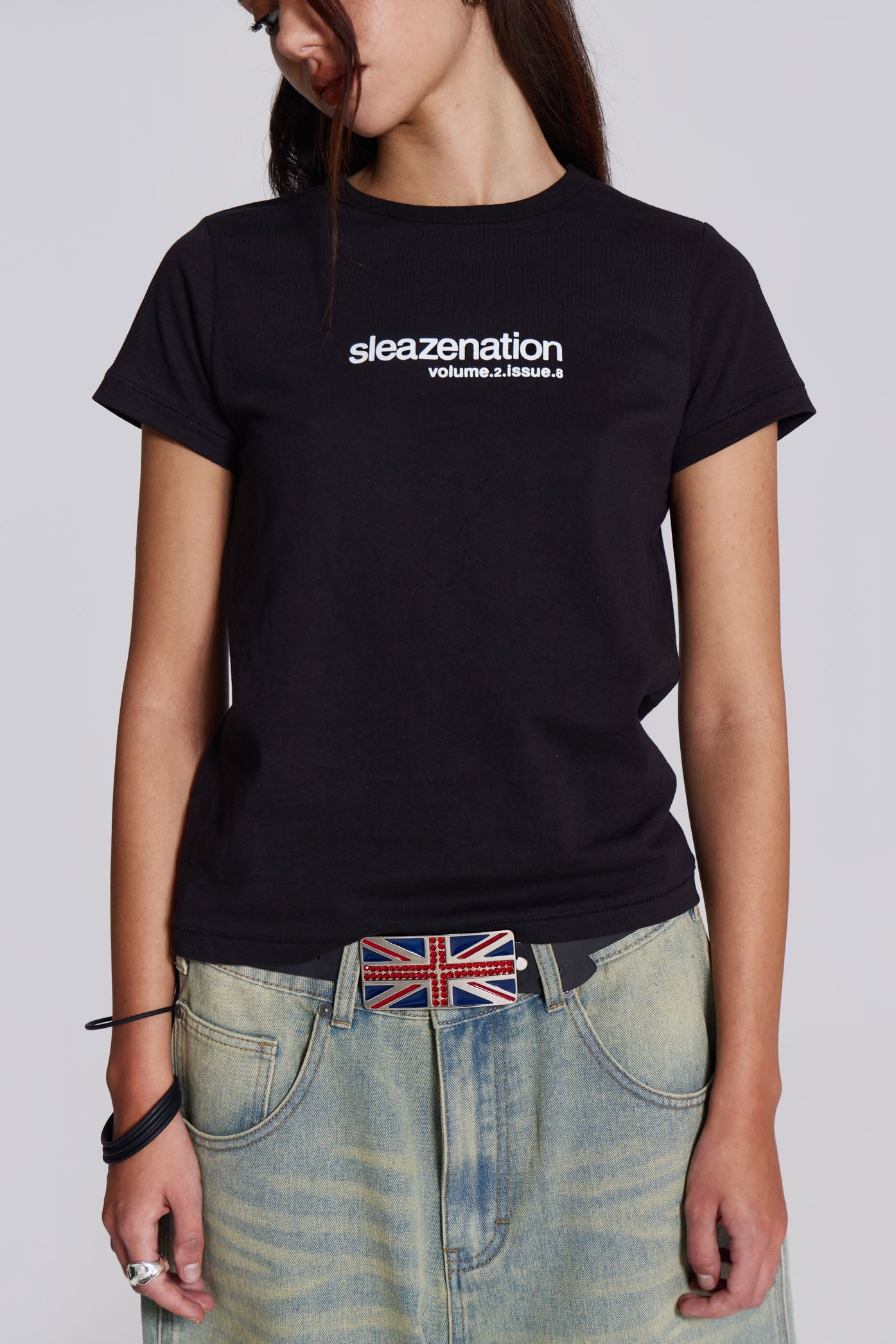 Woman wearing black slogan t-shirt, styled with blue denim jeans and union jack belt.