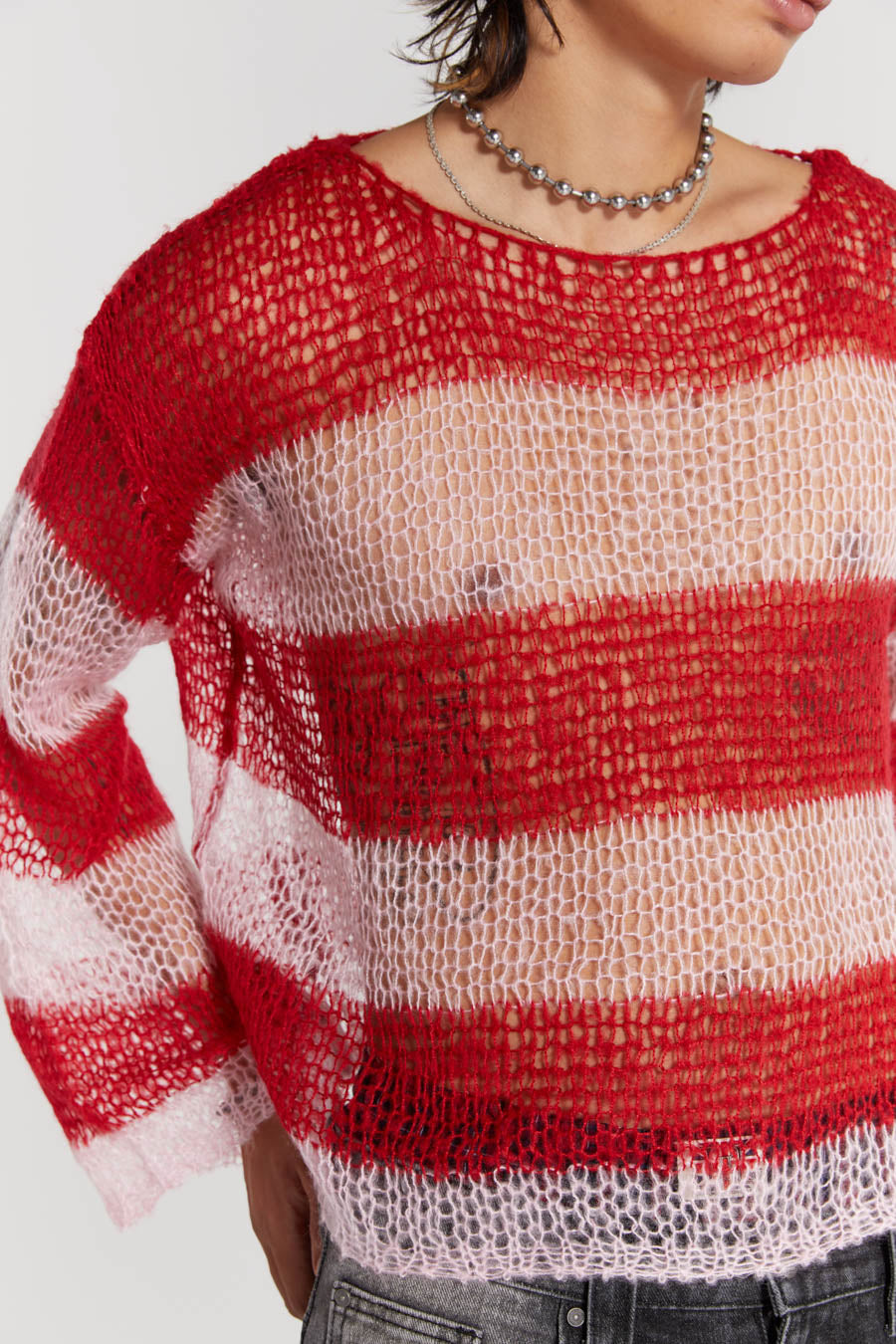 Male wearing red and pink striped loose fitted knitted jumper. Styled with black colossus jeans. 