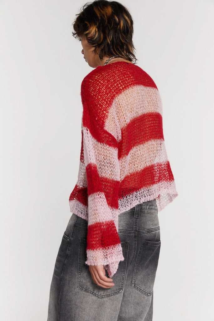 Male wearing red and pink striped loose fitted knitted jumper. Styled with black colossus jeans. 