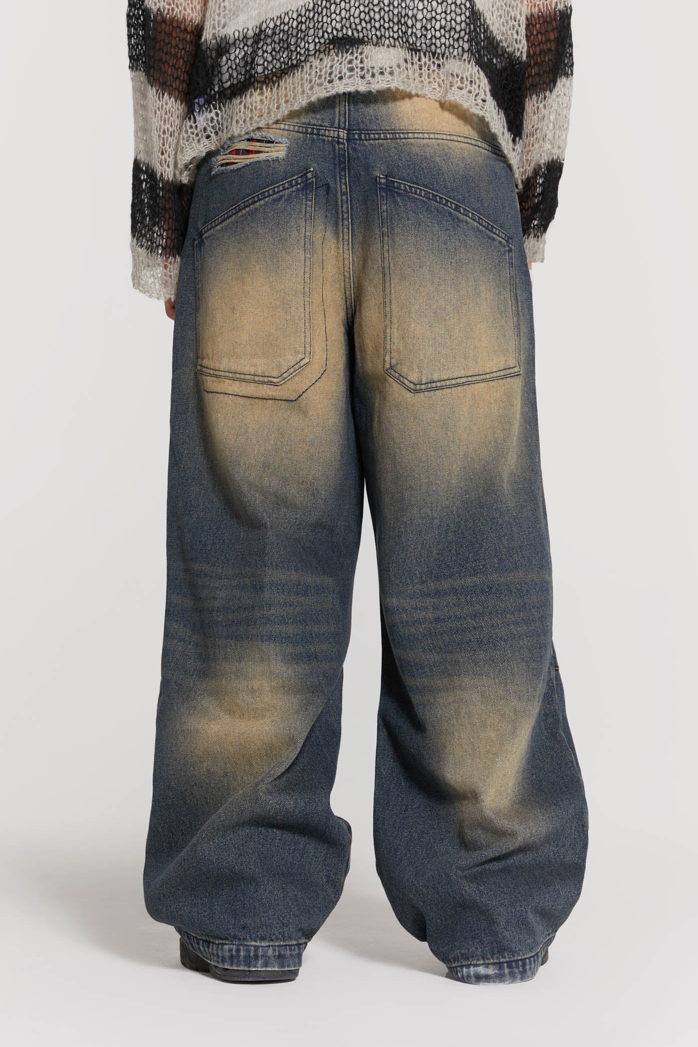 Male wearing sandblast blue denim jeans in a busted colossus mid-rise fit with double knee rips. Styled with a black and grey striped knit jumper. 