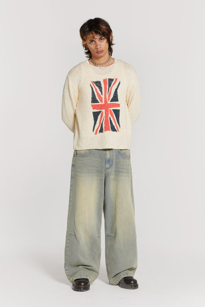 Male wearing blue light wash colossus fit jeans. Styled with white long sleeve knitted jumper with Union Jack print. 
